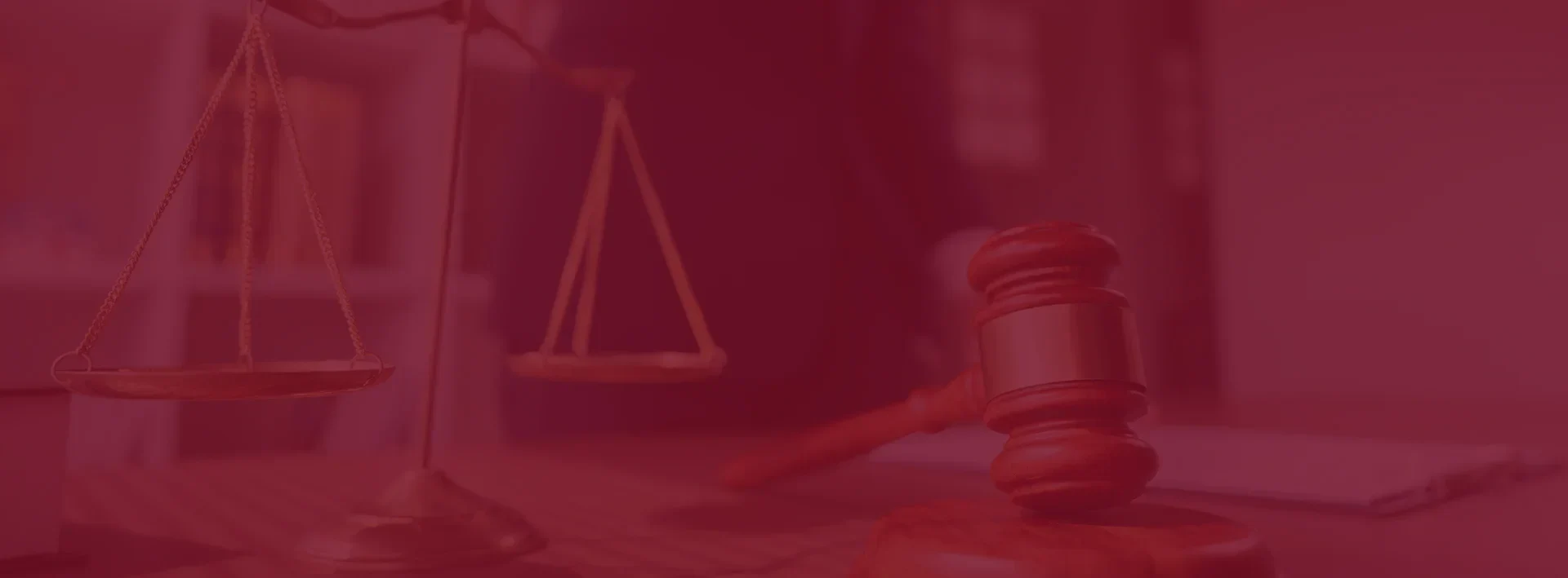 A judge's gavel and a scale of justice on a desk, with a blurred person in a suit in the background